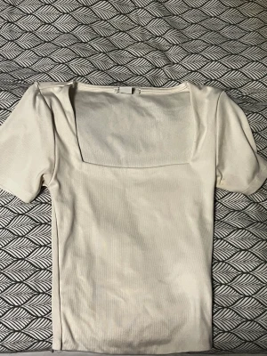 Vit topp med fyrkantig hals - Säljer en stilren vit topp från Amisu i storlek XXS. Toppen har korta ärmar, och en snygg fyrkantig halsringning som ger en modern vibe. Perfekt att matcha med jeans eller kjol för en clean look.