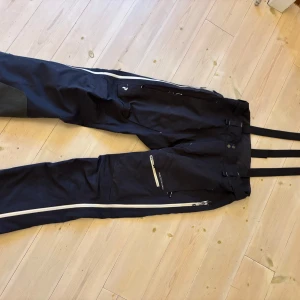 Mörkgråa täckbyxor Peak Performance XL - Peak Performance täckbyxor i storlek XL man. Mörkgrå färg med vita dragkedjor och hängslen. Byxorna har använts under flera säsonger och har diverse slitage men är fortfarande fullt funktionell. Modell: Alpine GORE-TEX C-Knit™ 3L Shell Pants Herr. Nypris: 6 500kr 