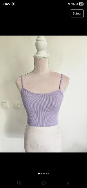 Ljuslila ribbad croppad linnetopp - Säljer en ljuslila croppad linnetopp med smala axelband och ribbad struktur. Toppen är figurnära och har en enkel, stilren design som är perfekt för varma dagar. Materialet känns mjukt och stretchigt mot huden.