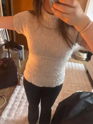 Säljer en beige stickad polotröja från Olsen med korta ärmar och snygga flätade detaljer. Tröjan har en hög, ribbad polokrage och är gjord i ett mjukt stickat material som känns skönt mot huden. Perfekt för dig som gillar en chill och stilren look.