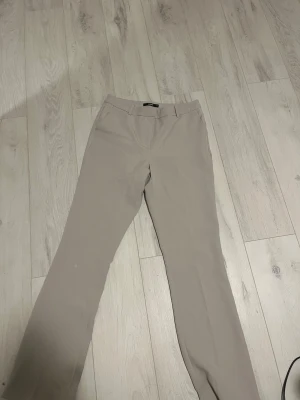 Beige kostymbyxor från Bik Bok - Snygga beige kostymbyxor från Bik Bok i storlek 44. Byxorna har raka ben, bälteshällor och diskreta fickor bak. Perfekt för en clean och stilren look. Använt dom två gånger nästan helt nya. Högmidjad. 