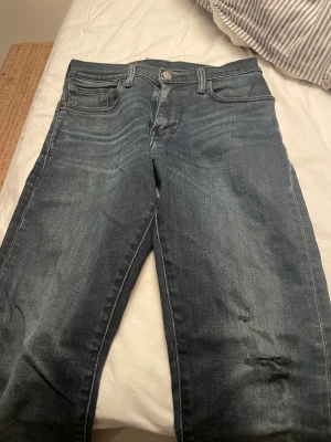 Levi's 512 mörkblå jeans slim fit - Snygga Levi's 512 jeans i mörkblå tvätt med klassiska fem fickor och slim fit passform. Jeansen har en lätt slitning på ena benet och detaljer som metallknappar och läderpatch bak. Perfekt för dig som gillar en modern och stilren look.