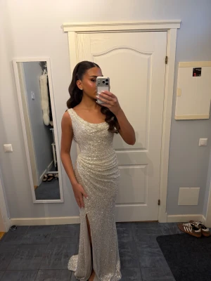 Silver glittrig långklänning  - Supersnygg långklänning i silver från Dressroom, täckt av glittrande paljetter. Klänningen har en draperad, figurnära passform med slits framtill och breda axelband. Perfekt för dig som vill sticka ut och glänsa på bal, bröllop eller fest! Använd 1 gång! Pris är diskuterbart!