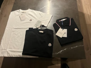 Moncler t-shirt och piké svart/vit - Tänkte vi kör en 3X bundle som många frågat efter. Finns olika storlekar. Två stilrena t-shirts och en pikétröja från Moncler. En vit t-shirt och en svart t-shirt med rund hals och Moncler-logga på bröstet. Svart piké med krage, vita och röda detaljer samt logga. Perfekt för dig som gillar exklusiva märken och enkel design.