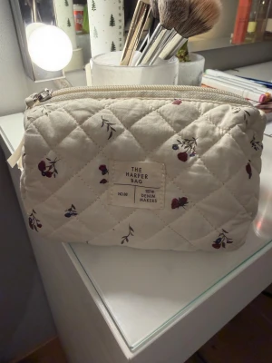 Liten necessär från Lager157 - Säljer en lite mindre necessär från Lager157. Perfekt storlek att ha i väskan. Den är krämvit och har ett sött mönster med röda blommor. Den är som ny men har några små fläckar inuti som det oftast blir. Hör gärna av dig vid frågor❤️