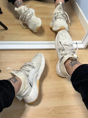 Adidas Tubular Rise vita sneakers - Säljer ett par Adidas Tubular Rise sneakers i ljusbeige och vitt med stickad ovandel och chunky sula i gummi. Skorna har snörning och detaljer i mocka och syntet, samt en unik design med högt skaft och dragflik bak. Perfekta för dig som gillar streetstyle. Använda ca 3 gånger. Org pris 1000 kr. Kan eventuellt bli mycket renare om de tvättas. 