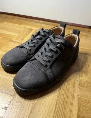 Christian Louboutin grå mocka sneakers - Snygga grå sneakers från Christian Louboutin i mocka med klassisk röd sula och rund tå. Skorna har snörning och en stilren, låg profil som passar till streetwear. Insidan är beige och sulan har Louboutin-loggan ingraverad. Kommer med box dustbag och kort 