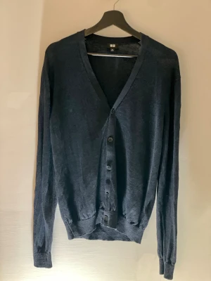 Mörkblå kofta från Uniqlo - Snygg mörkblå kofta från Uniqlo med v-ringning och knappar framtill. Lätt och tunn i materialet, perfekt för lager-på-lager. Långärmad och med ribbade muddar vid ärmslut och nederkant. Enkel och stilren design som funkar till många outfits.