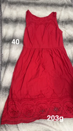 Röd ärmlös klänning med spetsdetaljer - Snygg röd klänning med ärmlös design och vackra broderade spetsdetaljer upptill och längs nederkanten. Klänningen har en feminin siluett och rundad halsringning, perfekt för dig som vill sticka ut med färg och detaljer.🌸 Fint använt skick. Storlek 40