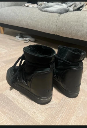 Svarta Inuikii boots i skinn och mocka - Säljer ett par svarta Inuikii boots med högt skaft, snörning och platt sula. Skorna är tillverkade i en mix av skinn och mocka, med en mysig insida och grova snören som ger en cool look. Perfekta för kalla dagar och passar till jeans eller leggings. Har nån skavank på sidan av skon men syns knappt! 