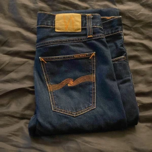Mörkblå jeans från Nudie Jeans - Snygga mörkblå jeans från Nudie Jeans med klassisk femficksdesign och kontrastsömmar i orange. Jeansen har raka ben, har normal passform och är använda fåtal gånger. W32/L32. Pris är 700 men kan diskuteras🍾💫