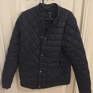 Mörkblå quiltad jacka Polo Ralph Lauren - Snygg mörkblå quiltad jacka från Polo Ralph Lauren. Storleken passar för 170-175.den är i ett otroligt bra skick har inga skador. Ny pris runt 1299kr.