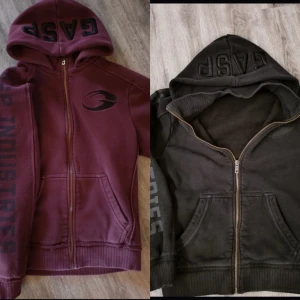 GASP hoodie med dragkedja - Två hoodies från GASP med broderad logga på huvan och tryck på ärmen. Ena är mörkröd och den andra svart, båda har hel dragkedja, huva och fickor framtill. Perfekt för dig som gillar sportig och avslappnad stil.