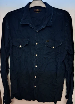 Mörkblå slim fit skjorta från Lee - Snygg mörkblå skjorta från Lee i slim fit-modell. Skjortan har långa ärmar, klassisk krage och två bröstfickor med knappar. Materialet är bomull och knäppningen framtill är med metallknappar. Perfekt för dig som gillar stilren denim-look.