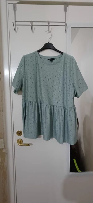 Ljusgrön blus med volang från Esmara - Säljer en ljusgrön blus från Esmara med korta ärmar och rund hals. Blusen har små prickar som mönster och en söt volang nedtill som ger en flowy känsla. Perfekt för dig som gillar en chill och feminin stil.