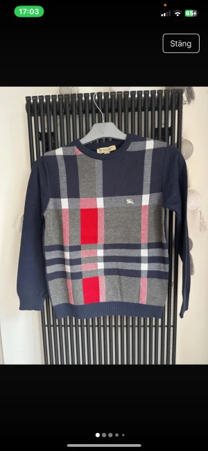 Rutig Burberry London tröja i bomull - Snygg långärmad tröja från Burberry London med klassiskt rutigt mönster i marinblått, grått, rött och vitt. Tröjan är gjord i mjuk bomull och har rund hals samt ribbade muddar. Perfekt för dig som gillar stilrena och ikoniska designer. Tröjan sitter lite mindre skulle säga att den passar dig perfekt om du är 152 