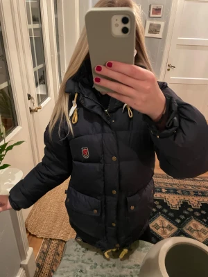  Fjällräven jacka - Säljer en mörkblå dunjacka från Fjällräven i storlek XS.  Men den passar även S. Det finns en defekt som bilden visar men det syns inte när man har på sig den!
