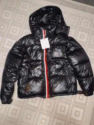 Svart Moncler pufferjacka med huva - Svart glansig pufferjacka från Moncler i storlek S. Jackan har huva, fickor med dragkedja och en cool rödvit rand längs dragkedjan. Moncler-logga på bröstet och quiltad design. Perfekt för dig som vill ha en snygg och varm jacka med street vibe.