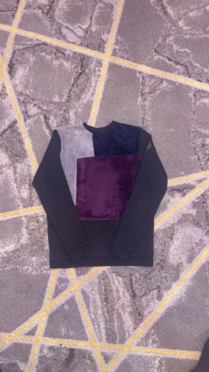 Blockmönstrad sammetströja i svart blå och  lila  - Cool långärmad tröja med blockmönster i svart, grått och mörklila sammet. Tröjan har en avslappnad passform och rund halsringning. Perfekt för dig som gillar unika detaljer och mjuka material.