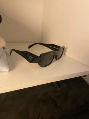 Parada solglasögon   - Svarta PRADA solglasögon . Modellen är SPR 17W-F och tillverkad i Italien. Glasögonen har en stilren och modern look. 