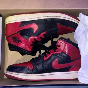 Nike Air Jordan 1 i svart och rött - Säljer ett par klassiska Nike Air Jordans i svart och rött. Skorna har snörning och är i bra skick med några tecken på användning. Perfekta för både vardag och sportiga tillfällen. Kommer i originalkartong. Skick 7,5/10