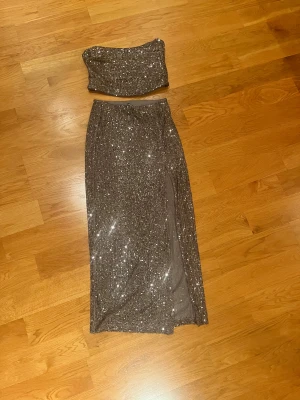 Glittrig långkjol och topp från ASOS DESIGN - Säljer en silverfärgad långkjol med topp från ASOS DESIGN med glittriga paljetter över hela kjolen. Kjolen har en snygg slits på sidan som ger extra edge och är perfekt för att sticka ut. Passformen är normal och materialet känns mjukt mot huden.