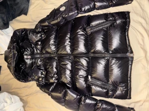 Svart Moncler pufferjacka  - Säljer brorsans moncler jacka, storlek 2. Utvändigt inga problem med jackan, däremot är serien lite sleten, loggan på knapparna har suddats ut lite och de är ett hål i vänster ficka!! Men den kommer hålla dig varm. Priset kan diskuteras!! 