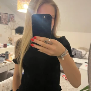 Svart ribbad topp med volangkant - Säljer en snygg ä svart ribbad topp med korta ärmar och volangkant nertill. Toppen har en croppad passform och är tillverkad i ett mjukt, stretchigt material. Liten till storleken där av  strl L