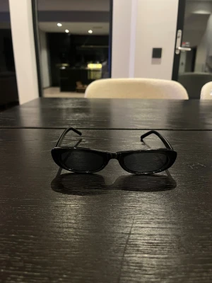 Svarta cat eye-solglasögon Saint Laurent - Snygga svarta solglasögon från Saint Laurent med cat eye-formade bågar. Tillverkade i Italien med glansig finish och diskret logga på skalmen. Perfekt accessoar för en trendig look.