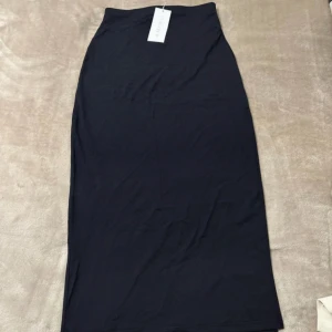 Svart långkjol från Amisu - Svart långkjol från Amisu med stilren och enkel design. Kjolen har en rak passform och är tillverkad i mjukt, stretchigt material som sitter skönt mot kroppen. Perfekt för dig som gillar minimalistisk stil och vill ha en kjol som är lätt att matcha med olika toppar.