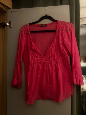 Rosa blus med v-ringning - Säljer en snygg rosa blus med djup v-ringning och veckade detaljer framtill. 
