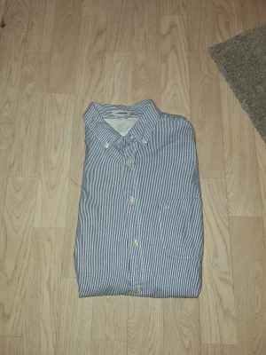 Randig skjorta från J.Lindeberg - Snygg skjorta från J.Lindeberg i regular fit med klassisk krage och knappar framtill. Skjortan har smala blå och vita ränder, bröstficka och är tillverkad i mjuk bomull. Perfekt för dig som gillar stilrena och fräscha plagg. Hör av er vid frågor eller prisförslag🙌🏼