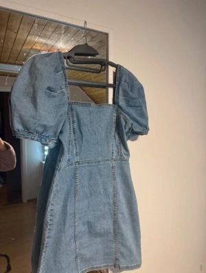 Kort jeansklänning med puffärmar - Säljer en snygg kort jeansklänning med puffiga kortärmar och fyrkantig halsringning. Har använt den bara två gånger!