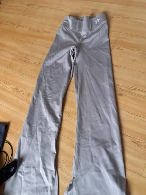 Grå träningsbyxor från Lager 157 - Snygga grå träningsbyxor från Lager 157 i storlek XS. De har hög midja och är gjorda i ett stretchigt syntetmaterial som sitter skönt mot kroppen. Byxorna har raka ben och en diskret logga framtill på linningen. Perfekta för gymmet eller yoga.