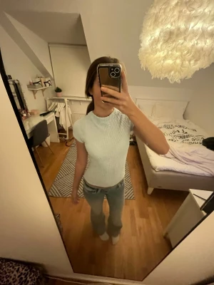 Ljusblå ribbad topp med kort ärm - Superfin ljusblå topp med korta ärmar och högre hals. Toppen har en ribbad, stretchig struktur som ger en cool och modern look. Perfekt att styla med jeans eller kjol för en fräsch vibe. Ändast and använd en gång!