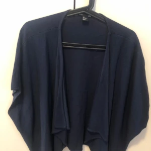 Mörkblå kofta från H&M - Säljer en mörkblå, öppen kofta från H&M. Koftan har en lös och avslappnad passform med långa ärmar och faller snyggt framtill. Perfekt att slänga över en t-shirt eller linne för en chill look.