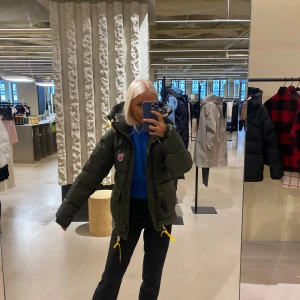 Grön pufferjacka från Fjällräven - Säljer en mörkgrön pufferjacka från Fjällräven med huva och gula dragskor. Perfekt jacka som verkligen håller värmen. Köpt ny från NK för 6999kr och är i fint skick. Inte använd supermycket och säljer pga jag ska köpa i en annan strl.