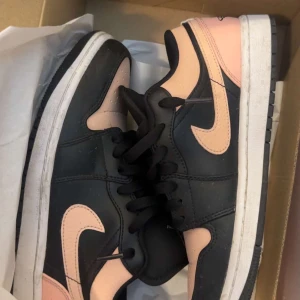 Nike Dunk Low svart och rosa - Nike Dunk Low sneakers i svart och ljusrosa med klassisk Swoosh på sidorna. Skorna har snörning, platt vit sula och rund tå. Materialet är skinn och syntet, perfekt för dig som gillar streetstyle och vill sticka ut med färgkombon.
