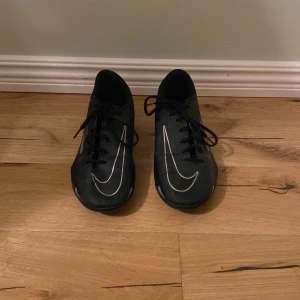 Nike Phantom fotbollsskor - Säljer ett par svarta Nike Phantom fotbollsskor med silverfärgade detaljer. Skorna har snörning och platt sula med dobbar för bra grepp på planen. Tillverkade i syntetmaterial för lätt känsla och snygg look. Använd ett få tal gånger, ca 5 gånger, väldigt snygga och sköna, storlek 38,5, priset kan diskuteras 