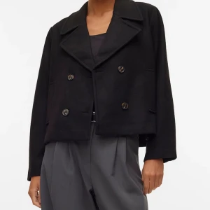 Svart kappa  - Stilren svart skepparkavaj från Vila med dubbelknäppning och bred krage. Jackan är croppad och har raka, långa ärmar samt två sidfickor. Perfekt för dig som gillar klassisk men trendig look. Slutsåld. Storlek S. Nytt pris 699.