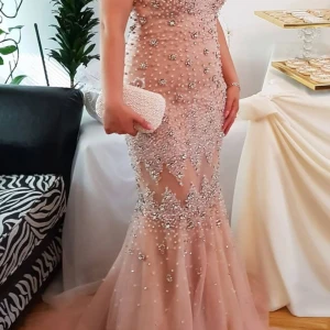 Champagnefärgad långklänning med paljetter - Säljer en magisk champagnefärgad långklänning med glittriga paljetter och pärlor över hela klänningen. Den har en v-ringad urringning, figurnära passform och ett skirt, utsvängt släp nedtill. Perfekt för bal eller nyår, du kommer verkligen sticka ut i denna!