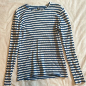 Randig långärmad tröja från pieces - Säljer en ribbad långärmad tröja med blå och vita ränder. Tröjan har en klassisk rund halsringning och är i mjuk bomull, perfekt för lager-på-lager eller som den är. Enkel och stilren vibe!