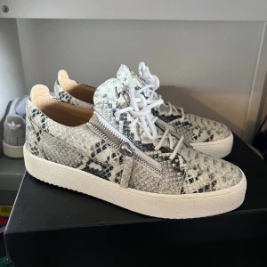 Giuseppe Zanotti sneakers i ormskinn - Snygga sneakers från Giuseppe Zanotti i vit och grå ormskinnslook med coola silverfärgade dragkedjor på sidorna. Skorna är i toppskick i princip nya. Oerhört stilrena och unika. Nypris ca 7k