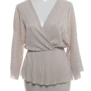 Beige omlottopp från Gina Tricot - Snygg beige omlottopp från Gina Tricot i storlek XS. Toppen har plisserat tyg, v-ringning och långa ärmar. Materialet är glansigt och känns lyxigt, perfekt för att lyfta din outfit. Passformen är normal och toppen har en lätt flowy känsla.