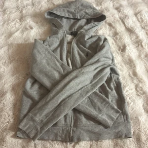 Grå hoodie från Polo Ralph Lauren XL - Grå hoodie från Polo Ralph Lauren i storlek XL. Klassisk design med dragkedja, huva och fickor framtill. Broderad logga på bröstet och mjukt bomullsmaterial som känns skönt mot huden. Perfekt för chill dagar eller när du vill ha en clean look.