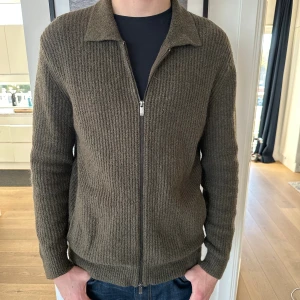 Grön stickad cardigan från Massimo Dutti - Säljer en olivgrön sällsynt stickad kofta cardigan från Massimo Dutti. Koftan har en snygg krage, hel dragkedja framtill och ribbad struktur. Perfekt för lager-på-lager och chill höststil. Grymt skick, inga defekter. Nypris 1999kr. Vårat pris 899kr. Storlek L. Modellen är 186 cm. Skriv vid minsta intresse!