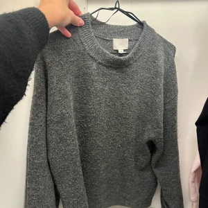 Grå stickad tröja från H&M - Mysig grå stickad tröja från H&M i storlek XS. Tröjan har en klassisk rund halsringning, lång ärm och är tillverkad i ett mjukt stickat material som passar perfekt för kyligare dagar.