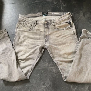 Replay anbass jeans - Snygga grå jeans från Replay i slim fit-modell. Jeansen har klassisk femficksdesign, dragkedjegylf och diskreta slitningar för en cool look. Materialet är mjukt denim och färgen är ljusgrå med lätt tvättad effekt.  Jeansen har lite defekter som ni kan se i bilderna. Den där slags färgen på byxorna går nog bort i tvätten kan tvätta dom innan du köper dom. Kom med frågor och funderingar😆 priset kan vi ändra i snabb afär🤗
