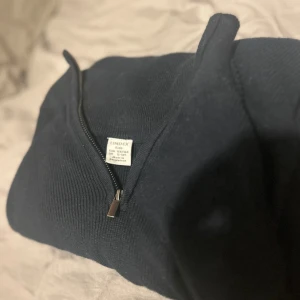 Svart stickad half zip-tröja Lindex - Mörkblå stickad tröja från Lindex med half zip-dragkedja och långärmad design. Tröjan har en enkel och clean look, perfekt till jeans eller andra casual outfits. Materialet är mjukt och ribbat för extra komfort.