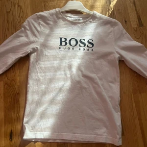 Vit långärmad tröja Hugo Boss - Vit långärmad tröja från Hugo Boss med svart logotyptryck på bröstet. Klassisk rund halsringning och rak passform. Tillverkad i mjuk bomull, perfekt för en clean och stilren look. Sitter bra på folk med storlek 138. Kan även diskutera pris.